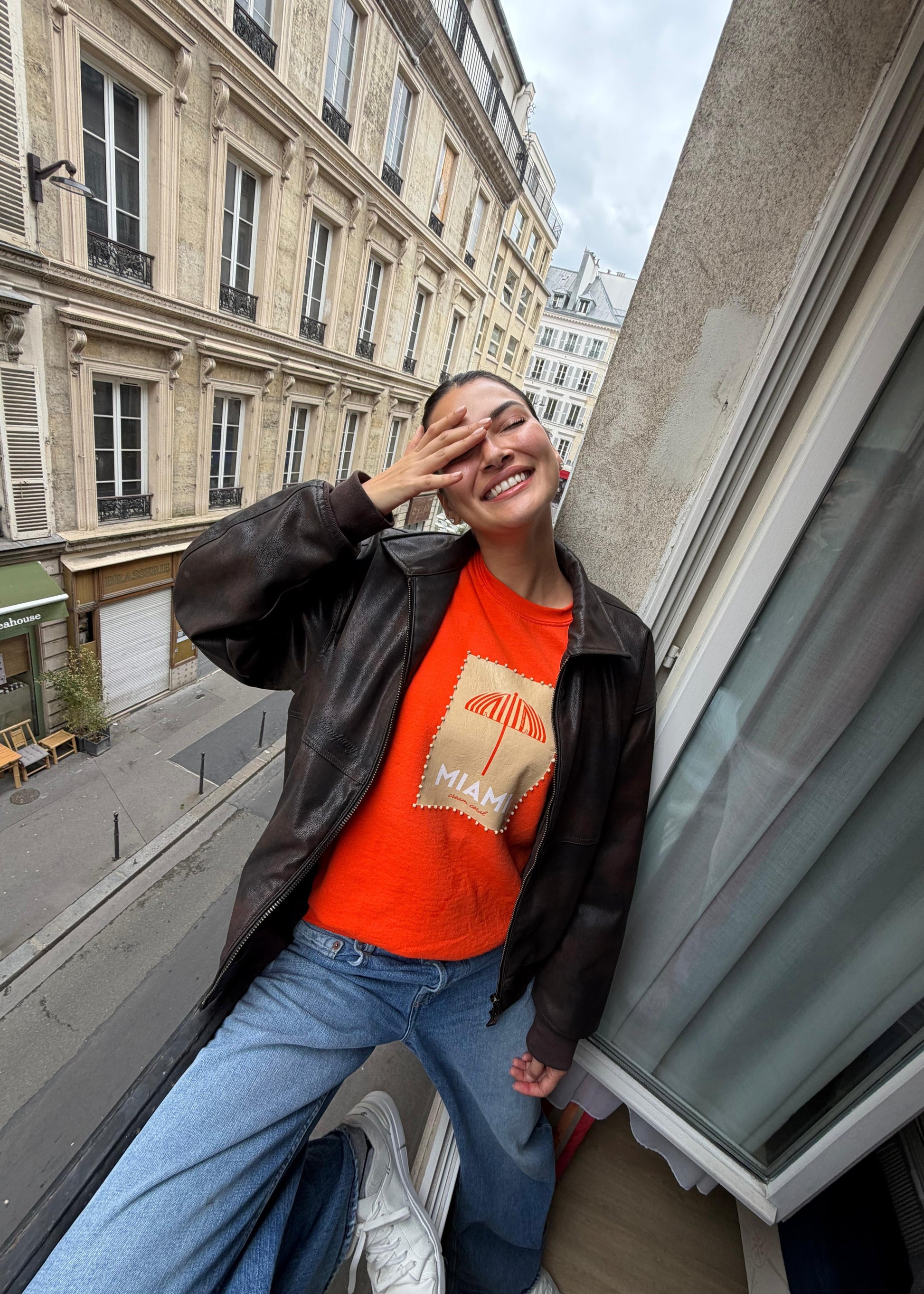Person wearing an orange shirt with a graphic design, sitting on a ledge in an urban setting.